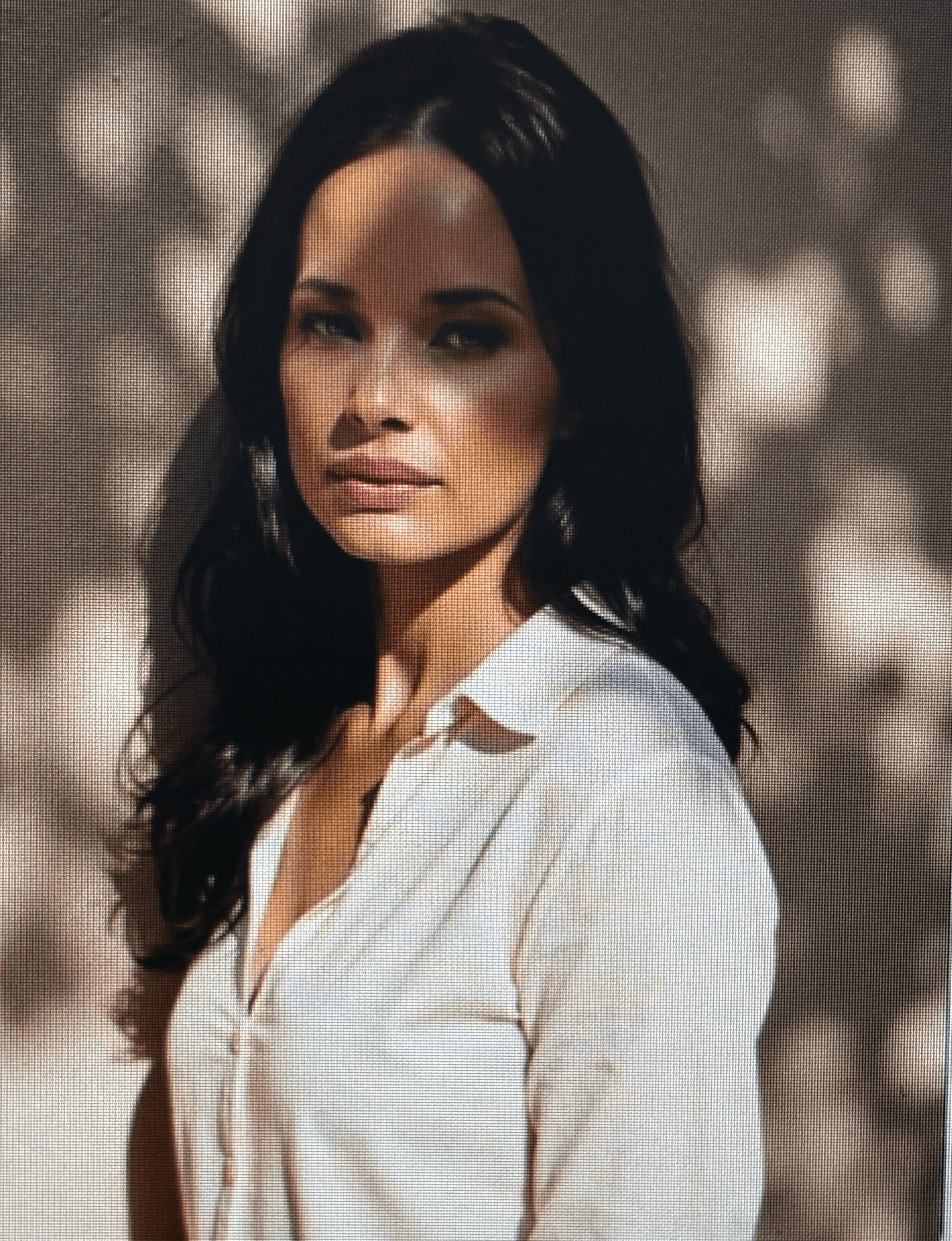 Woman with long dark hair wearing a white shirt under dappled sunlight and shadows.
